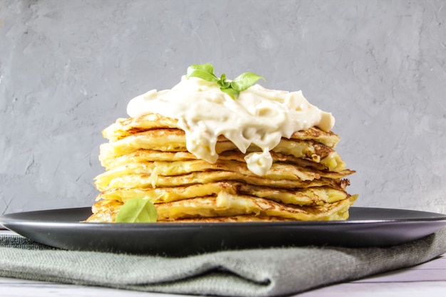 Vegetarian zucchini pancakes servered with cream sauce and basil leaves on a black plate Vegan food