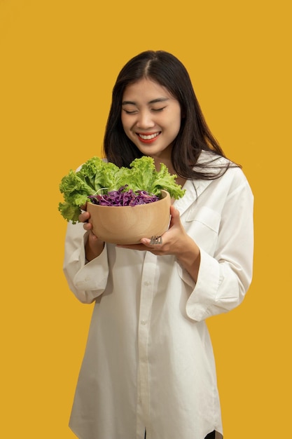 Vegetarisch concept Gezonde vrouw die mengelings verse groentesalade op geïsoleerde gele achtergrond eet