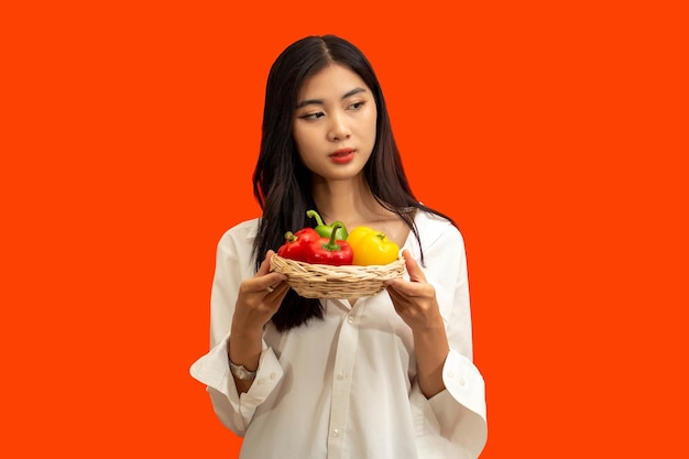 Vegetarisch concept Gezonde vrouw houdt mand met kleurrijke paprika geïsoleerd op oranje achtergrond