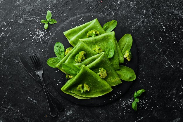 Vegetarisch eten Groene Spinaziepannenkoekjes met groenten op een zwarte stenen plaat Bovenaanzicht Vrije ruimte voor uw tekst