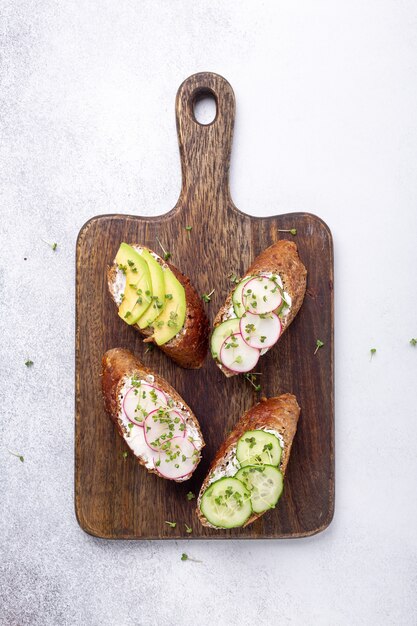 Vegetarische broodjes op een houten bord. roomkaas, avocado, komkommer, radijs en mosterd microgreens. bovenaanzicht. gezonde snack