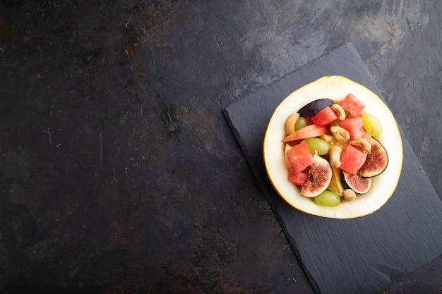 Vegetarische fruitsalade van watermeloen, druiven, vijgen, peer, sinaasappel, cashew op leisteen bord.