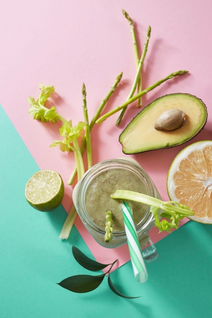 Vegetarische gezonde smoothies van groene groenten met groene bladeren, schijfjes citroen, avocado, komkommer en plastic rietje in een glazen kom op duotone roze groen papier achtergrond. Bovenaanzicht.