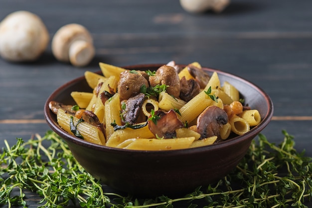 Vegetarische pasta met champignons, kikkererwten, spinazie, specerijen en kruiden. Italiaanse pasta in een kom op een oude houten tafel.