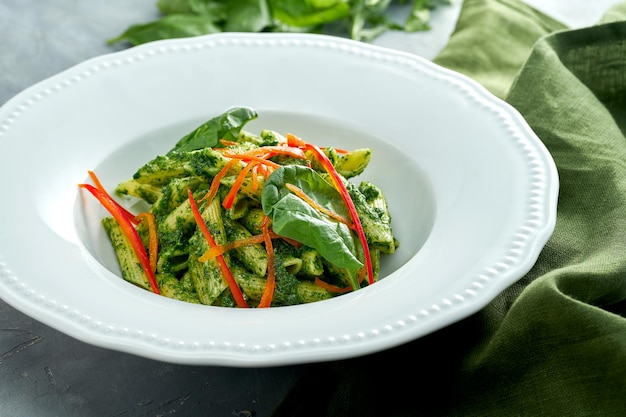 Vegetarische pasta met spinazie en peper in een witte plaat op een grijze achtergrond