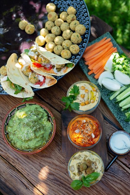 Vegetarische picknick op een houten eiken tafel, hummus, falafel, pita, groenten, spinazie, basilicum en pestosaus met zonnebloempitten. Gezond Mediterraans eten.