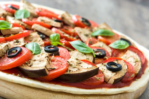 Vegetarische pizza met aubergine, tomaat, zwarte olijven, oregano en basilicum op houten tafel