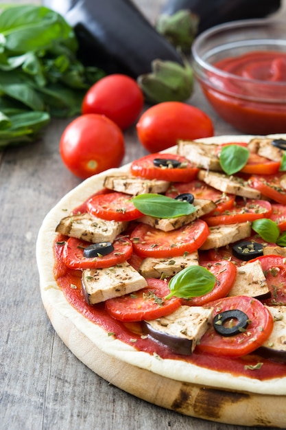 Vegetarische pizza met aubergine, tomaat, zwarte olijven, oregano en basilicum op houten tafel