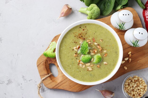 Vegetarische roomsoep met broccoli, spinazie en courgette in witte kom op grijze achtergrond. Bovenaanzicht. Ruimte voor tekst