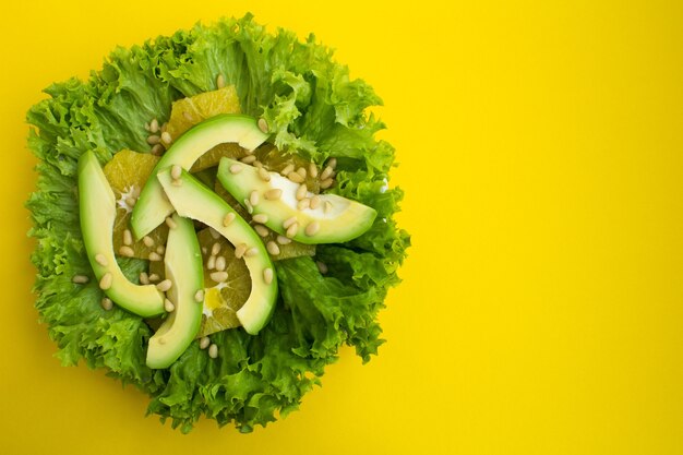 Vegetarische salade met avocado, slablaadjes, sinaasappel en pijnboompitten op de gele achtergrond.