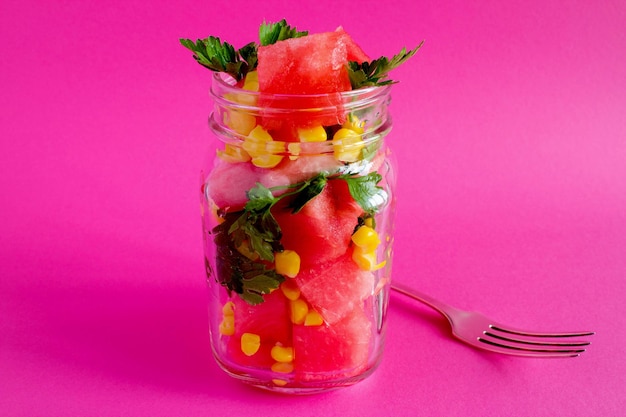 Vegetarische salade met watermeloen en maïs in de glazen pot op de roze achtergrond