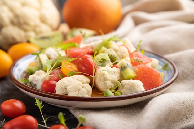 Vegetarische salade van bloemkool, kiwi, tomaten, microgroene spruiten op zwarte concrete achtergrond. Zijaanzicht, selectieve aandacht.