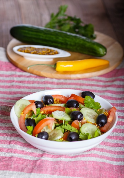 Vegetarische salade van tomaten, komkommers, peterselie, olijven en mosterd op linnen tafelkleed.