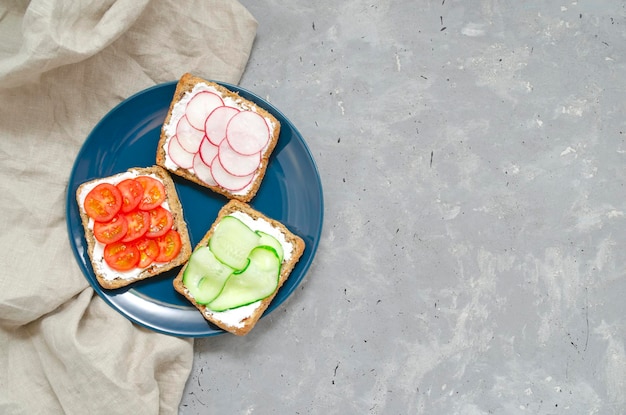 Foto vegetarische sandwiches met roomkaas verse komkommer radijs tomaten op een blauw bord