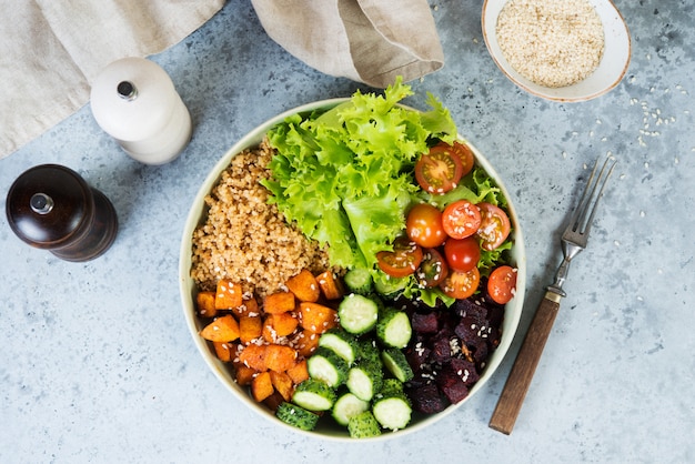 Vegetarische schotel een kom van gezonde quinoa met verse en gebakken groenten op een grijze betonnen achtergrond.