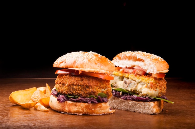 Veggie burger breaded with red cabbage tomato lettuce and rustic potatoes under wooden table