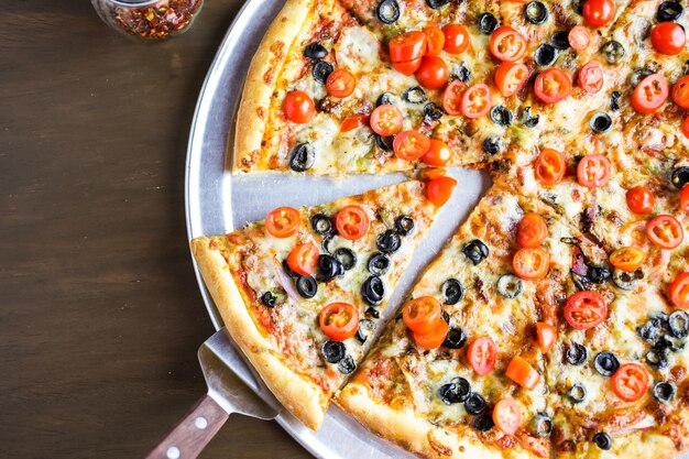 Veggie pizza with olives and cherry tomatoes on the table.