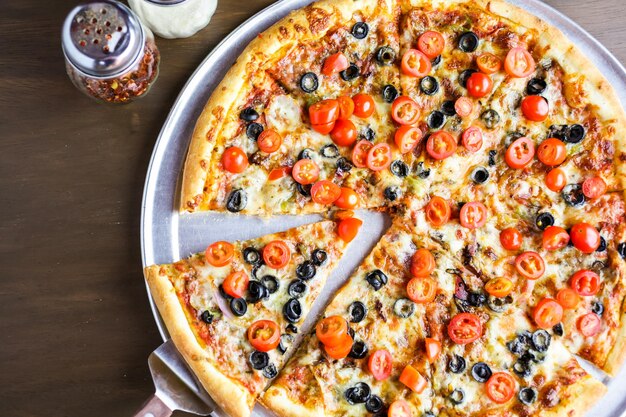 Veggie pizza with olives and cherry tomatoes on the table.