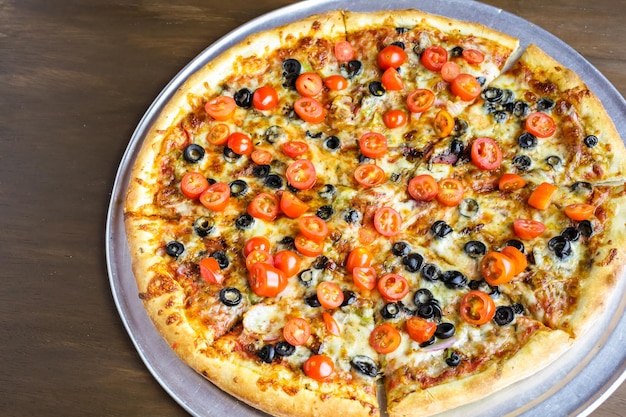 Veggie pizza with olives and cherry tomatoes on the table.