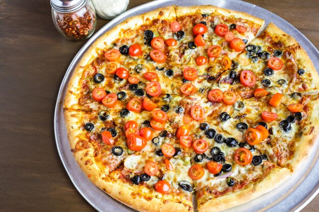 Veggie pizza with olives and cherry tomatoes on the table.