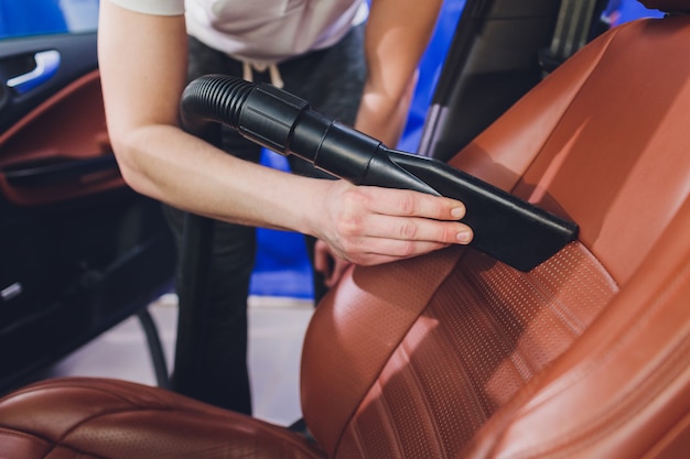 Vehicle interior vacuum cleaning. Detail shot of an industrial vacuum cleaner cleaning a car seat.