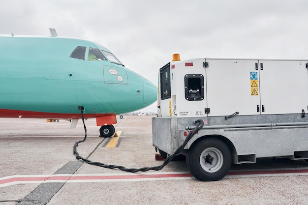 Photo vehicle nearby turboprop aircraft parked on the runway at daytime