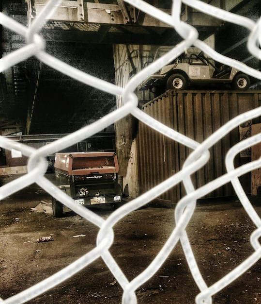 Vehicles and cargo container at factory seen through chainlink fence