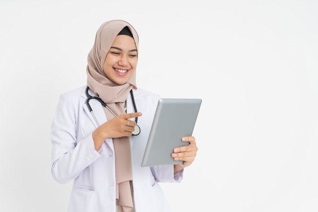 Photo veiled female doctor wearing white suit uniform smiling with finger pointing when looking at pad scr...