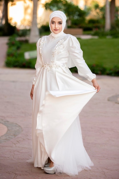 A veiled model stands holding her white dress and looking at the camera