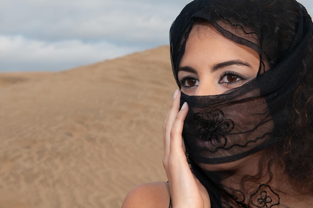 Veiled muslim arabic woman in desert dunes at sunset