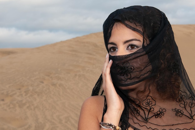 Veiled muslim arabic woman in desert dunes at sunset