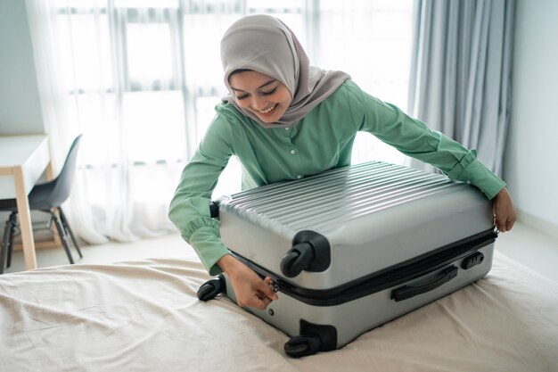 Veiled woman trying to close her full suitcase