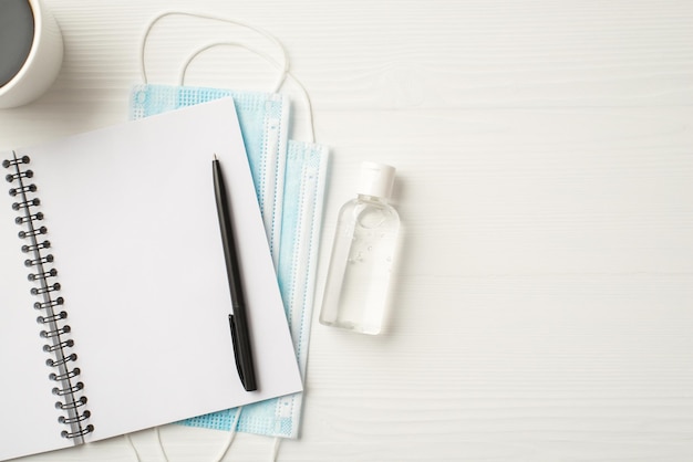 Veilig werkplekconcept. Top flatlay foto van mok mokka open heldere notebook pen stapel maskers en antiseptische geïsoleerde witte houten achtergrond