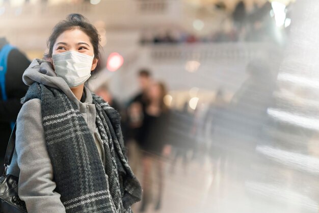 Foto veiligheid reizen jonge aziatische vrouwelijke reiziger draagt gezichtsmasker beschermende staande glimlach in treinstation met sociale afstand achtergrond nieuwe normale levensstijl