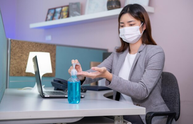 Veiligheid werkplekconcept Jonge zakenvrouw die gezichtsmasker draagt en Sanitizer handgel gebruikt