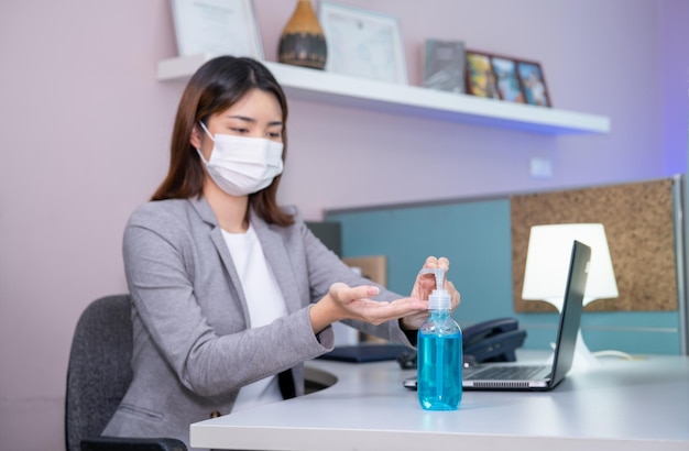 Veiligheid werkplekconcept Jonge zakenvrouw die gezichtsmasker draagt en Sanitizer handgel gebruikt