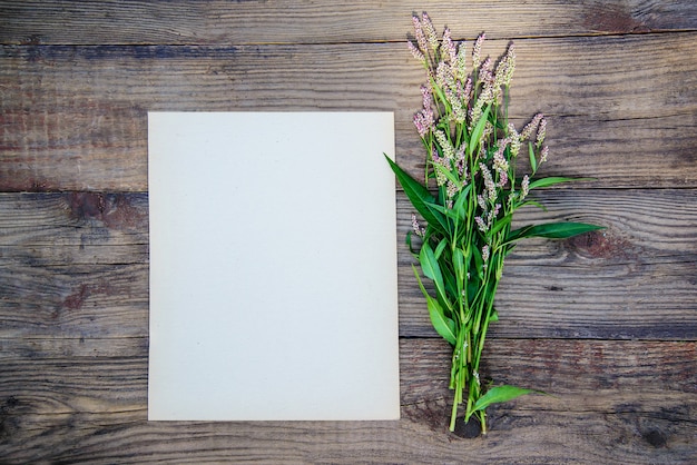 Vel papier en de kleine roze bloemen op houten achtergrond