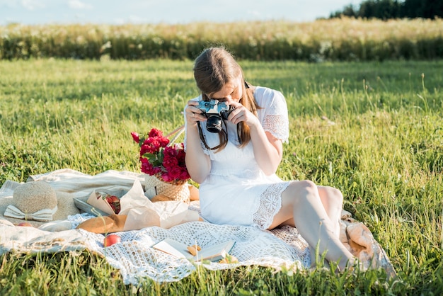 Veld in madeliefjes, een boeket bloemen. Romantische picknick in Franse stijl. Vrouw in katoenen jurk. Maakt foto's, fotograaf, aardbeien, croissants, bloemen op deken. Buitenbijeenkomst.