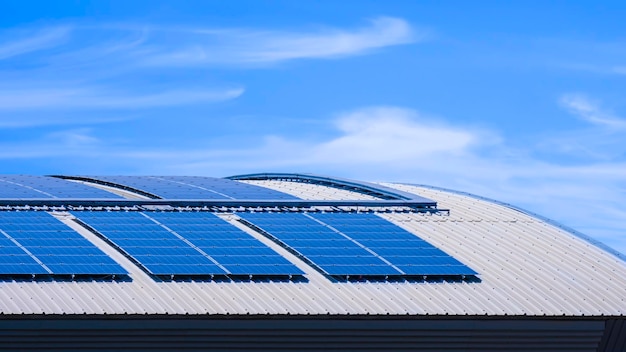 Vele zonnepanelen bovenop gebogen staaldak van industrieel gebouw tegen blauwe hemelachtergrond