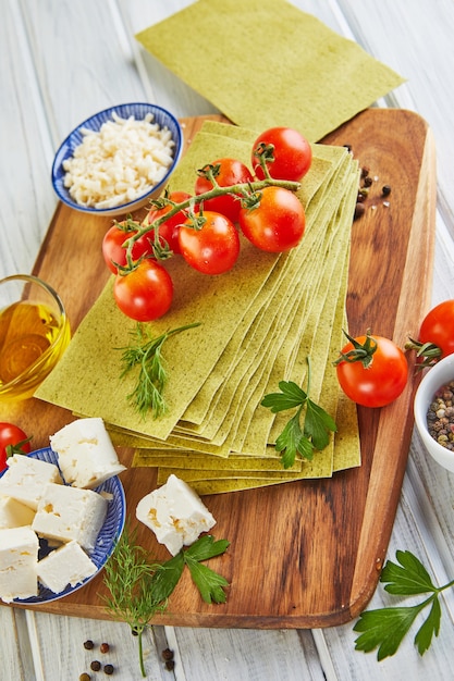 Vellen voor het maken van lasagne met spinazie en ingrediënten: kerstomaatjes, kaas, boter, paprika en kruiden.