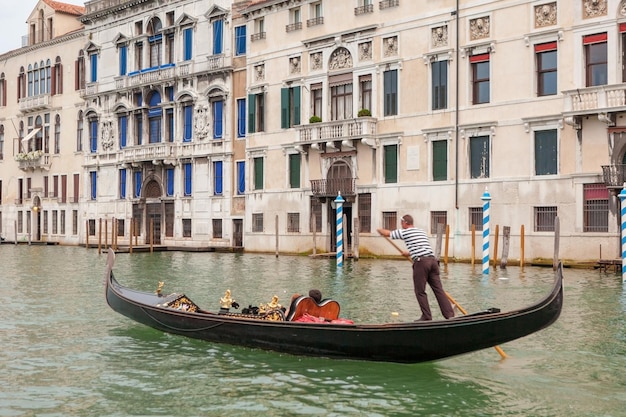 Venetiaanse gondelier punteren gondel door groene kanaalwateren van Venetië, Italië