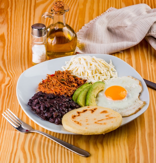 Venezolaans ontbijt van arepa, gebakken ei, zwarte bonen, mechada vlees, witte kaas en avocado