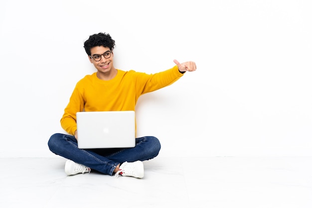 Venezolaanse man zittend op de vloer met laptop met een duim omhoog gebaar