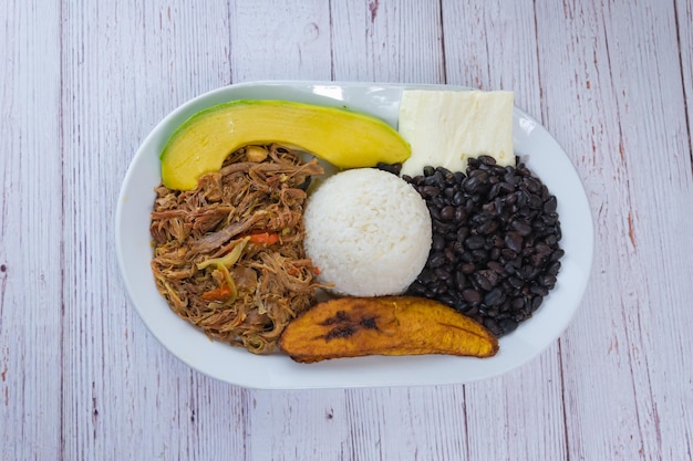 Foto venezolaanse pabellon crillo rijstkaas zwarte bonen versnipperd vlees avocado en gebakken plantain