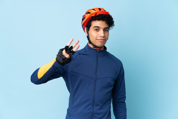 Venezuelan cyclist man isolated on blue background happy and counting three with fingers