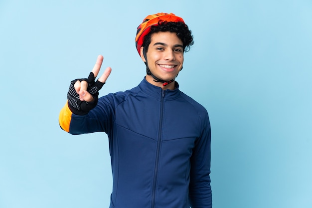 Venezuelan cyclist man isolated on blue background smiling and showing victory sign