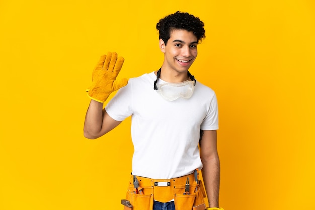 Venezuelan electrician man on yellow saluting with hand with happy expression