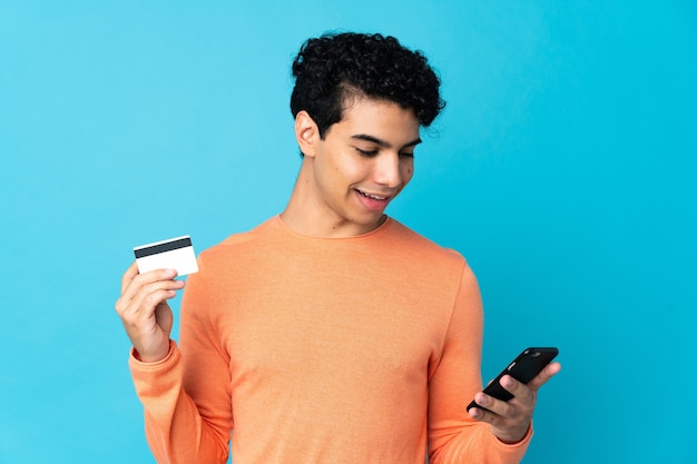 Venezuelan man isolated on blue buying with the mobile with a credit card