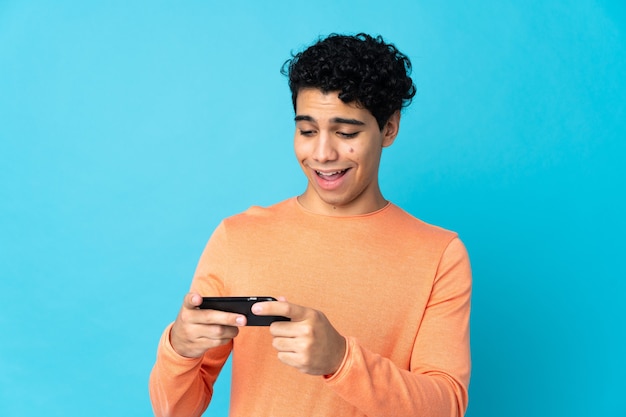 Venezuelan man isolated on blue playing with the mobile phone