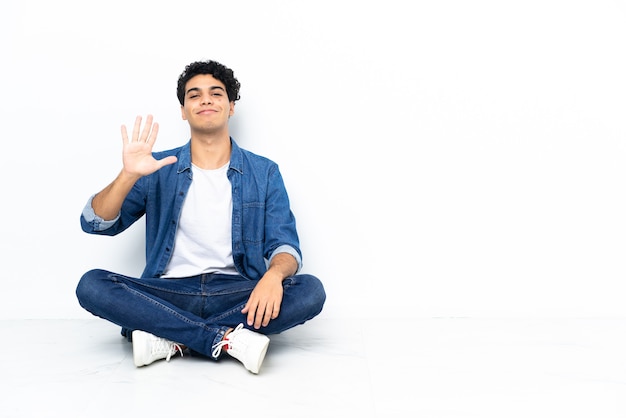 Venezuelan man sitting on the floor counting five with fingers